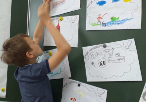 Do tablicy szkolnej przyczepione są rysunki dzieci z podpisem „Moje marzenie”. Uczeń przyczepia do tablicy kartkę, na której narysował swoje marzenia.